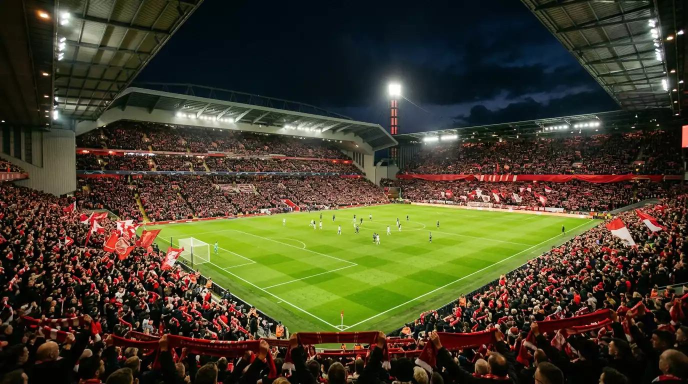 Estadio de fútbol con césped verde iluminado bajo focos nocturnos y banderines rojos en las gradas